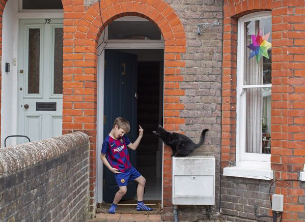 Юный футболист на пороге своего дома и соседский кот, заглядывающий через дверь, Великобритания - Sputnik Латвия