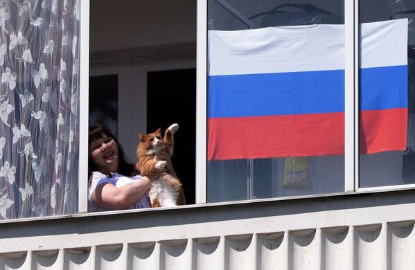 Жительница Красноярска со своим котом смотрит выступление музыкального ансамбля в День России из окна своей квартиры - Sputnik Латвия