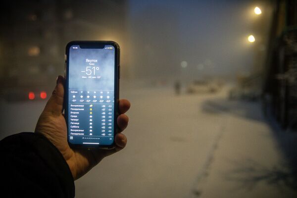 Мужчина демонстрирует мобильный телефон с информацией о прогнозе погоды в Якутске - Sputnik Латвия