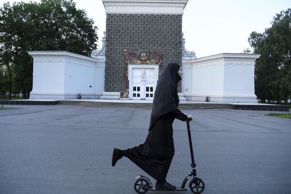 Женщина в хиджабе катается на скутере перед зданием с символикой Советского Союза во Всероссийском выставочном центре в Москве Женщина в хиджабе катается на скутере перед зданием с символикой Советского Союза во Всероссийском выставочном центре в Москве - Sputnik Latvija
