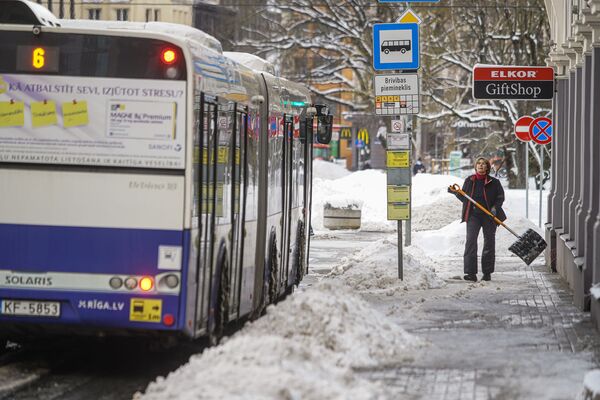Женщина убирает снег на остановке общественного транспорта - Sputnik Latvija