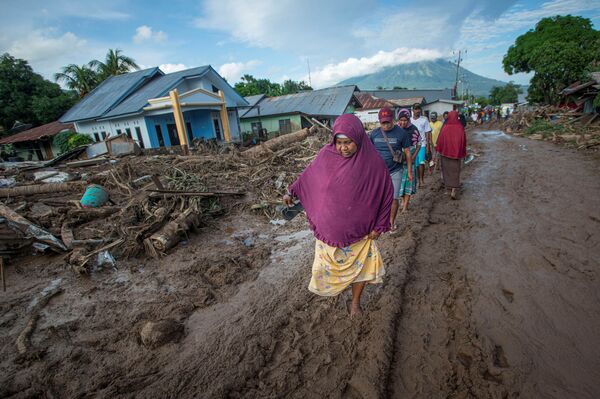 Cilvēki soļo pa dubļiem Austrumnusas-Tengaras provincē Indonēzijā pēc tropiskā ciklona uzobrukuma - Sputnik Latvija