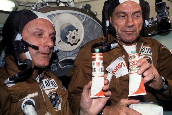 Американские астронавты Томас Стаффорд и Дональд Кент «Дик» Слейтон с тюбиками советской еды в орбитальном модуле Союз. На контейнер с борщом приклеена наклейка водка. - Sputnik Латвия