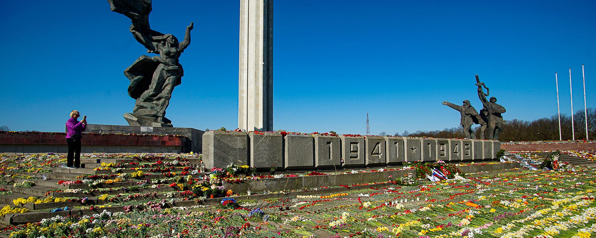 Женщина фотографирует цветы, разложенные у памятника Освободителям Риги - Sputnik Латвия, 1920, 05.05.2022