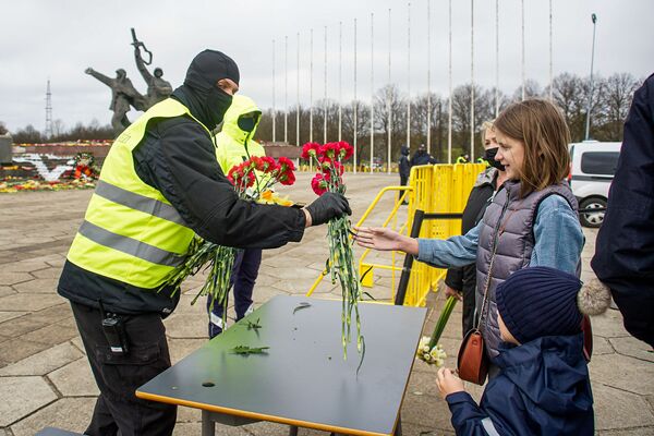 Cilvēki atstāj ziedus uz galdiem netālu no pieminekļa, pēc tam ziedus nes uz monumentu Cilvēki atstāj ziedus uz galdiem netālu no pieminekļa, pēc tam ziedus nes uz monumentu - Sputnik Latvija