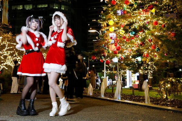 Santa Klausa tērpā ģērbtās meitenes pozē Ziemassvētku iluminācijas fonā Tokijā. - Sputnik Latvija