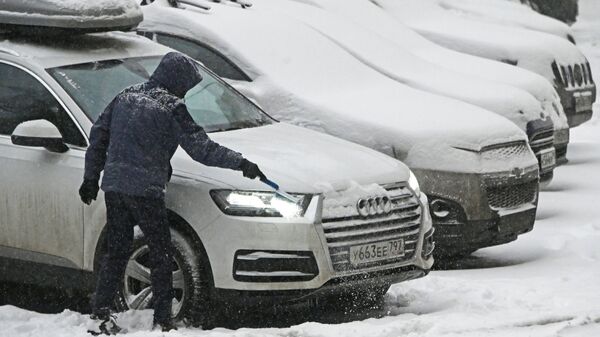Мужчина чистит от снега свою машина во время снегопада в Москве - Sputnik Латвия