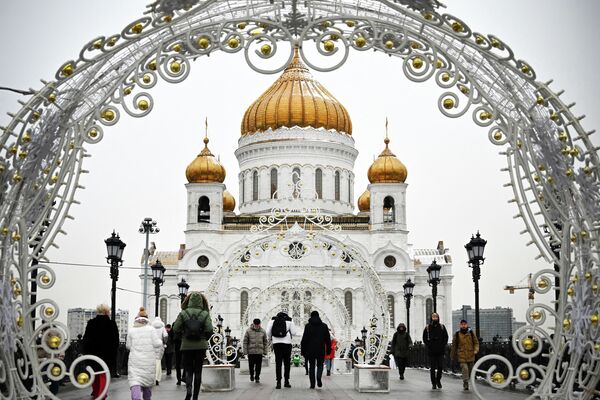 Пешеходы проходят через рождественские украшения перед Храмом Христа Спасителя, главным русским православным храмом, в Москве. - Sputnik Латвия
