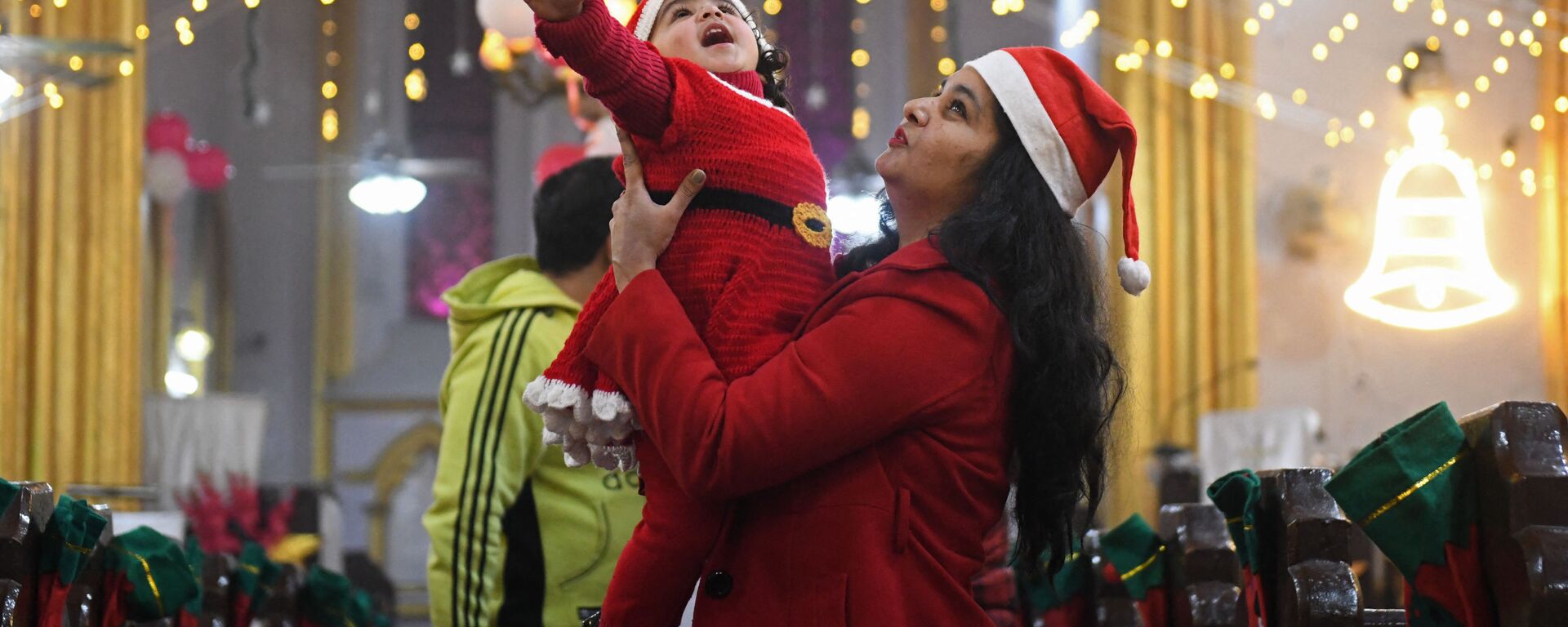 Мать держит ребенка в костюме Санта-Клауса накануне Рождества в церкви Святого Павла в Амритсаре, Индия - Sputnik Латвия, 1920, 25.12.2021