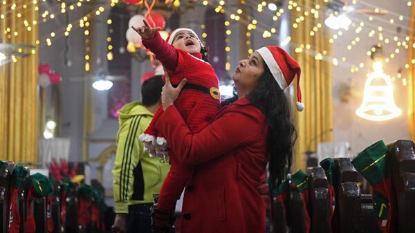 Мать держит ребенка в костюме Санта-Клауса накануне Рождества в церкви Святого Павла в Амритсаре, Индия - Sputnik Latvija