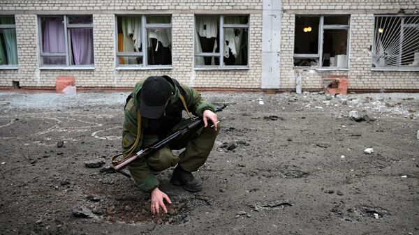 Сотрудник Народной милиции ДНР возле воронки от снаряда у школы Горловки - Sputnik Латвия