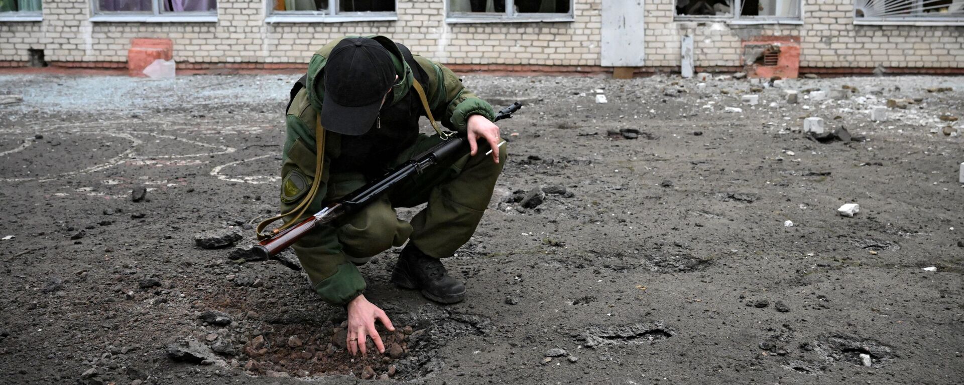 Сотрудник Народной милиции ДНР возле воронки от снаряда у школы Горловки - Sputnik Латвия, 1920, 04.03.2022