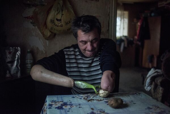 51 gadu vecais Jurijs Janušs, zaudējis rokas jau pirms kara, tīra kartupeļus. Vientuļiem invalīdiem nekādas lielās cerības nav, veselības aprūpi nesaņemt, darba nav. Regulāras apšaudes ir realitāte, kurā spiesti dzīvot cilvēki, kam arī miera laikā neklātos viegli - Sputnik Latvija
