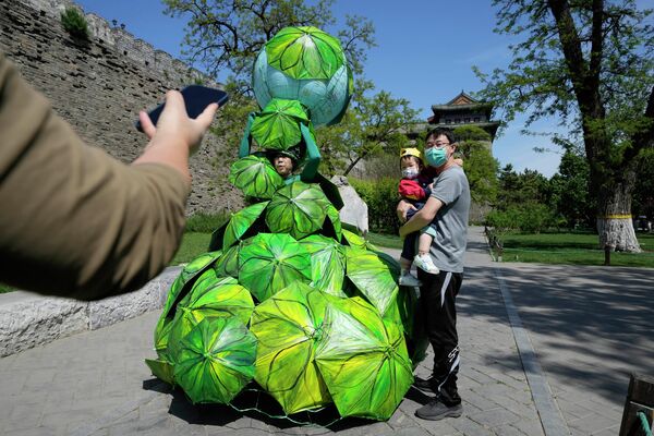 Мужчина с ребенком фотографируются рядом с работой под названием &quot;Защитите Землю с помощью зонтиков из банановых листьев&quot; китайской художницы Конг Нин  - Sputnik Латвия