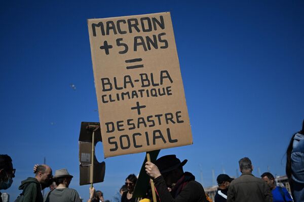 Протестующий держит плакат с надписью &quot;Макрон + 5 лет = климатическое бла-бла-бла + социальная катастрофа&quot; во время ежегодного Первомая (Дня труда). Марсель, юг Франции, 1 мая 2022 года. - Sputnik Латвия