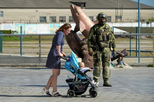 Sieviete ar bērnu ratiņiem Hersonas krastmalā līdzās Krievijas karavīriem - Sputnik Latvija