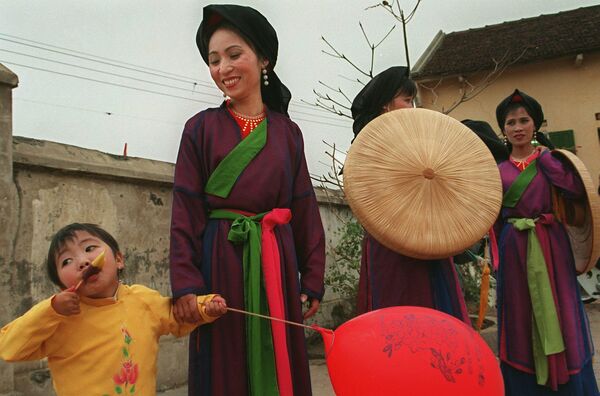 Девочка лакомится мороженым рядом с артистами в традиционных костюмах, исполняющими песни во вьетнамском стиле &quot;Куан хо&quot; в провинции Бакнинь, 10 февраля 1998 года.   - Sputnik Латвия