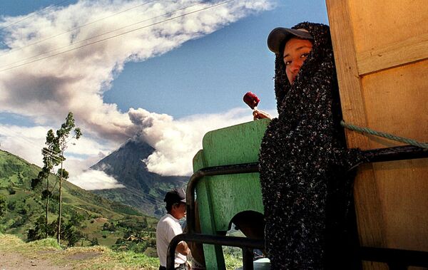 Женщина ест мороженое, в то время как вулкан Тунгурауа изрыгает пепел и дым рядом с ней в Патате, Эквадор, 11 ноября 1999 года. - Sputnik Латвия
