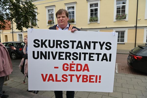 Участник акции протеста держит плакат с надписью: &quot;Бедствующие университеты — позор государству!&quot;. - Sputnik Латвия