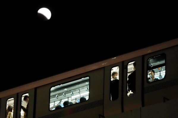 Люди едут в поезде во время лунного затмения в Токио. - Sputnik Латвия