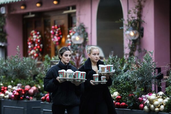 Две женщины несут напитки из Starbucks на празднично украшенной улице британской столицы. - Sputnik Латвия