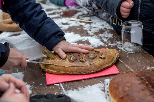 Мужчина разрезает пирог с начинкой из целой рыбы с торчащим хвостом на конкурсе-дегустации национальной карельской выпечки на рыболовном фестивале Пудожские налимы - Sputnik Латвия