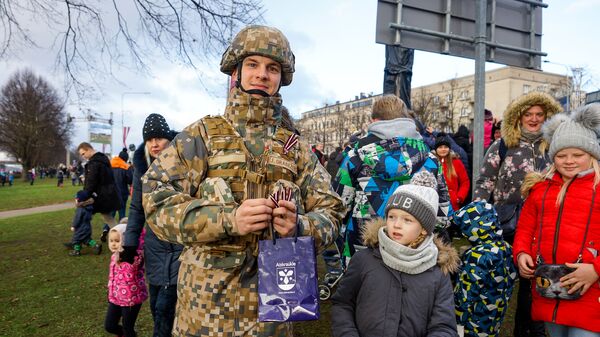 Латвийский военный раздает ленточки в цветах латвийского флага на параде в честь столетия Латвии - Sputnik Латвия