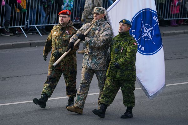 Немецкий, латвийский и канадский военные с флагом Расширенной передовой группы НАТО в Латвии - Sputnik Латвия