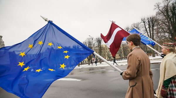 Юноша и девушка в национальных латышских костюмах с флагами ЕС и Латвии у Памятника Свободы в Риге - Sputnik Латвия
