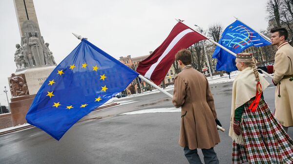 Юноша и девушка в национальных латышских костюмах с флагами ЕС и Латвии у Памятника Свободы в Риге - Sputnik Латвия
