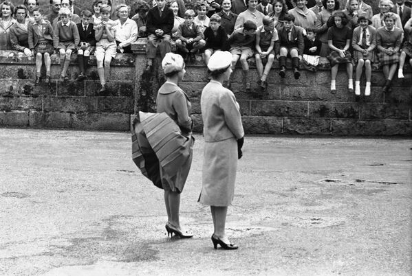 Ветер поднимает юбку принцессы Маргарет, пока они с королевой Елизаветой Второй ожидают прибытия президента США Дуайта Эйзенхауэра в замке Балморал, Шотландия - Sputnik Латвия
