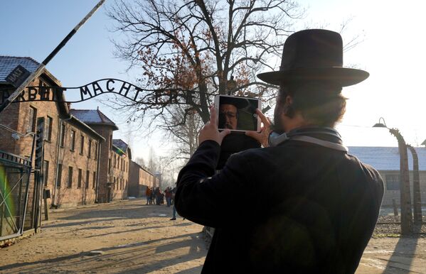 Посетитель музея Аушвиц-Биркенау в Освенциме фотографирует знаменитую надпись Arbeit macht frei на входе - Sputnik Латвия