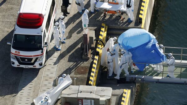 Сотрудники полиции в защитных костюмах помещают в машину скорой помощи заболевшего пассажира круизного лайнера Diamond Princes, помещенного в карантин у японского порта Йокогама - Sputnik Латвия