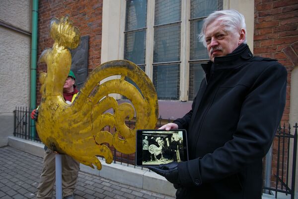 Юрис Дамбис, руководитель Государственной инспекции по охране памятников культуры, демонстрирует фото 1982 года, когда он принимал участие в реставрации этого петушка (на фото второй слева) - Sputnik Латвия