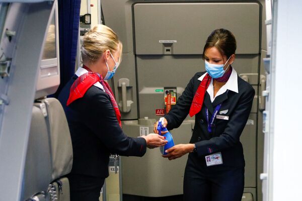 Стюардессы в медицинских масках обрабатывают руки антисептическим гелем в салоне самолета в международном аэропорту Брюсселя - Sputnik Латвия
