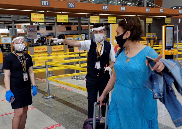 Сотрудники авиакомпании Pegasus Airlines в защитных масках и экранах указывают пассажиру нужное направление в международном аэропорту имени Сабихи Гекчен в Стамбуле - Sputnik Латвия
