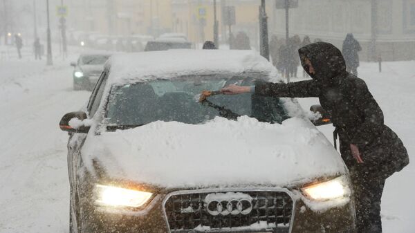 Владелица отчищает свою машину от налипшего снега во время снегопада в Москве - Sputnik Латвия