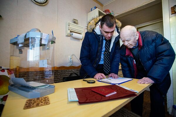 Член мобильной избирательной бригады объясняет пенсионеру правила голосования - Sputnik Латвия