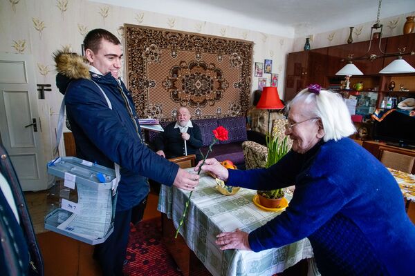 Член мобильной избирательной бригады дарит цветок участнице голосования Член мобильной избирательной бригады дарит цветок участнице голосования - Sputnik Латвия