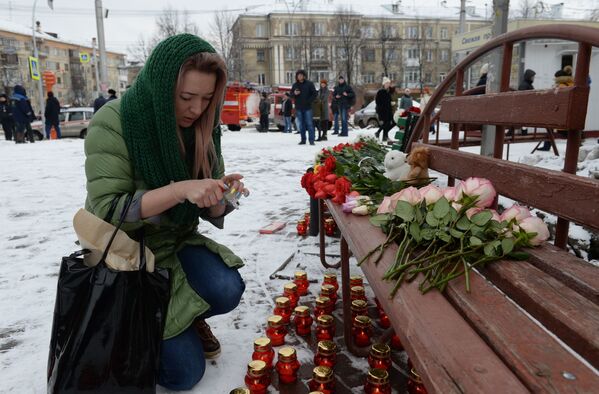 Женщина зажигает свечу возле здания торгового центра Зимняя вишня в Кемерове, где произошел пожар - Sputnik Латвия