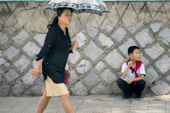 Девушка с зонтиком проходит мимо сидящего мальчика в Пхеньяне - Sputnik Латвия