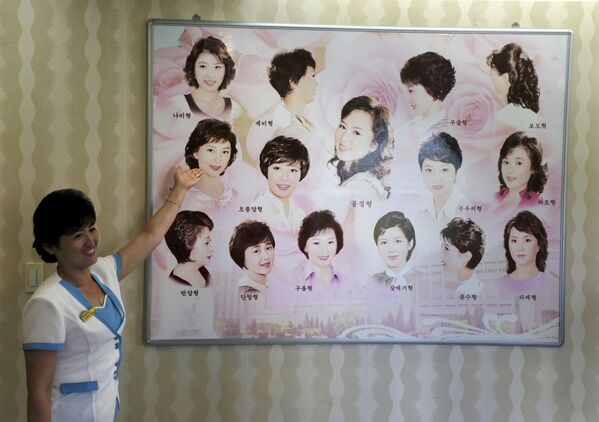 Гид показывает плакат с женскими прическами в парикмахерской Пхеньяна, Северная Корея - Sputnik Латвия